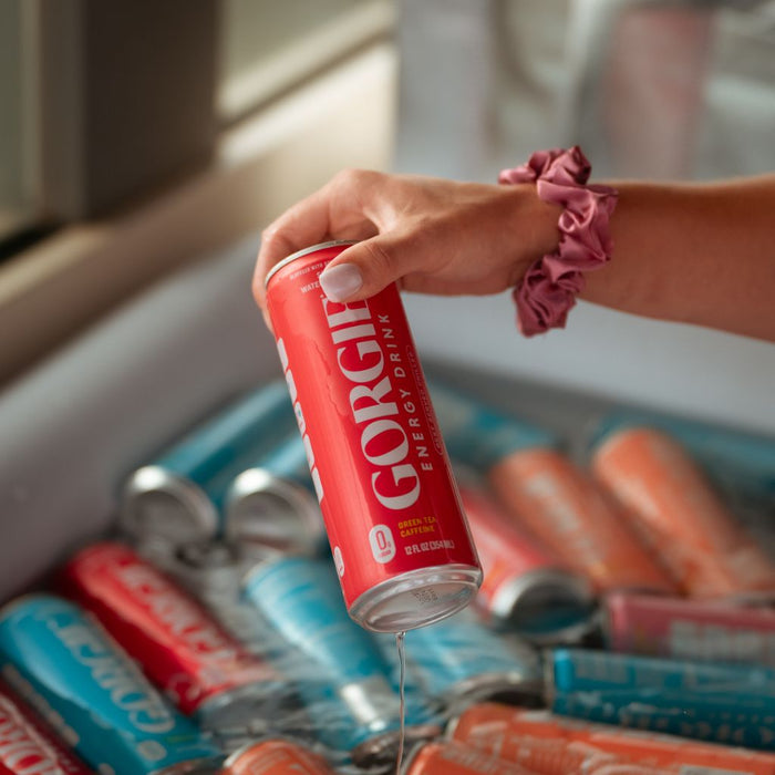 A hand holding a wet, cold red Gorgie energy drink can over an ice-filled cooler during a summer rooftop event in San Diego. - Sip & Social Club San Diego event