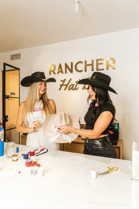 Two women designing and branding a custom rancher hat at the Coastal Cowgirl DIY workshop in San Diego.