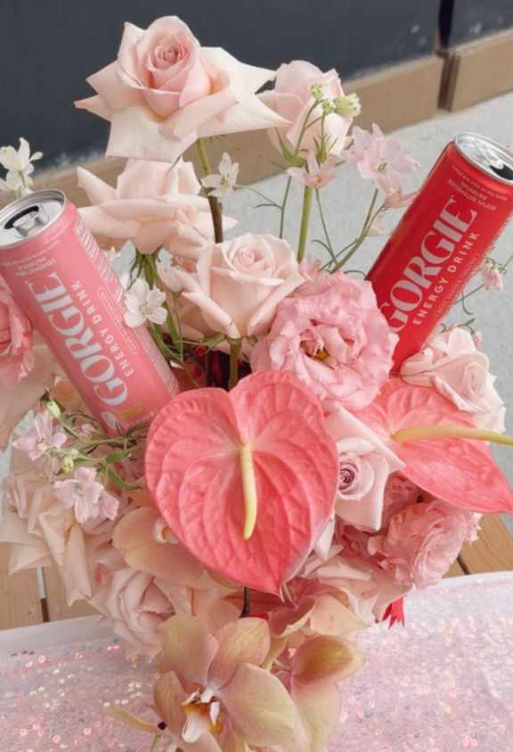 Red and pink Gorgie energy drink cans beautifully arranged within a pastel rose and orchid floral centerpiece at a Sip and Social event. - Sip & Social Club San Diego event