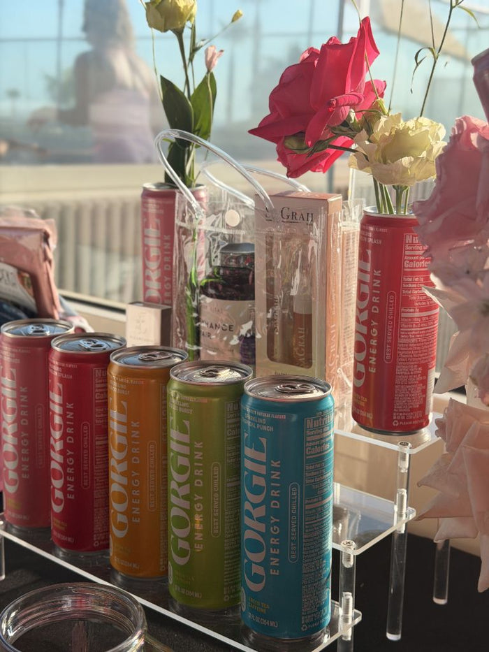 Colorful Gorgie energy drink cans displayed on clear acrylic stands with gift bags and flowers at a San Diego wellness pop-up. - Sip & Social Club San Diego event