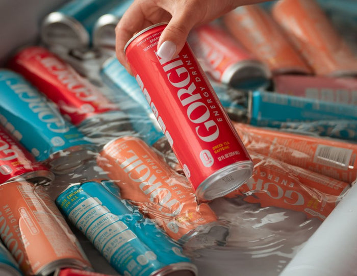 Close-up of a hand grabbing a cold red watermelon-flavored Gorgie energy drink can out of a container of ice water. - Sip & Social Club San Diego event