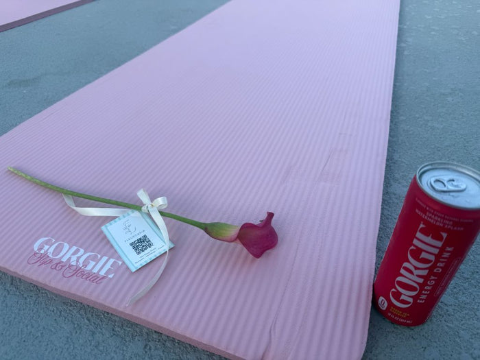 A single pink flower with a gift tag lying next to a red Gorgie energy drink can on a pink yoga mat at a San Diego rooftop pilates event. - Sip & Social Club San Diego event