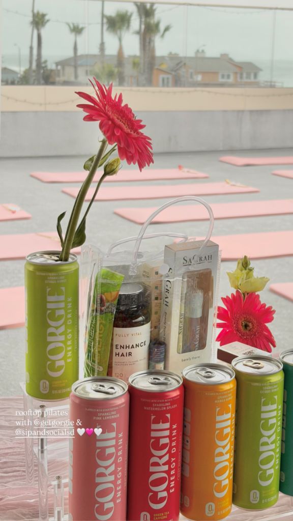 Colorful cans of Gorgie energy drinks lined up next to a clear gift bag filled with wellness products on a rooftop pilates deck in San Diego. - Sip & Social Club San Diego event