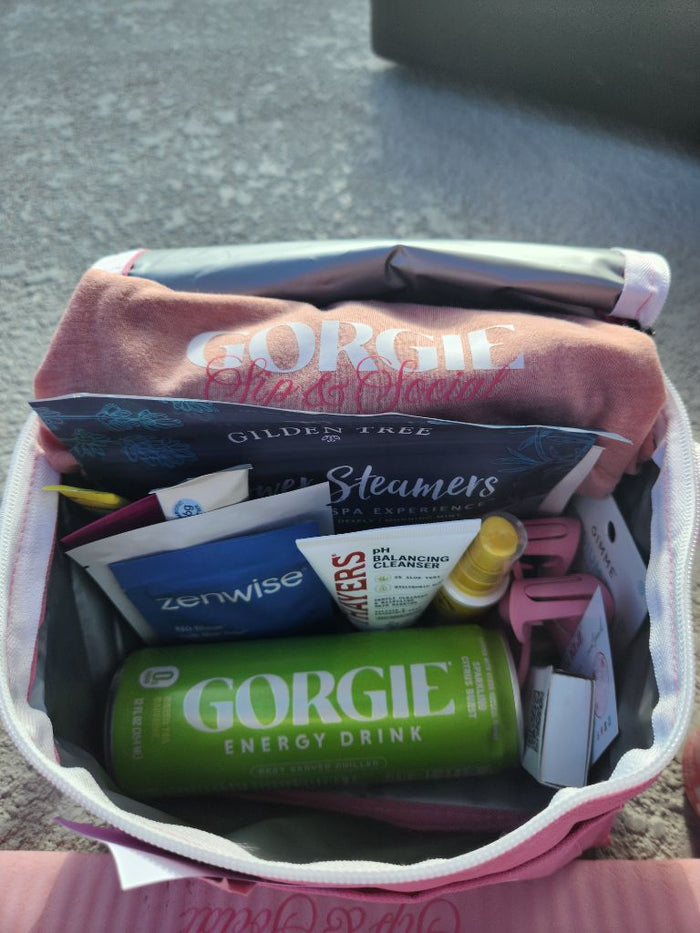 An open pink swag bag containing a green Gorgie energy drink, face cleanser, and skincare items on a rooftop deck in San Diego. - Sip & Social Club San Diego event