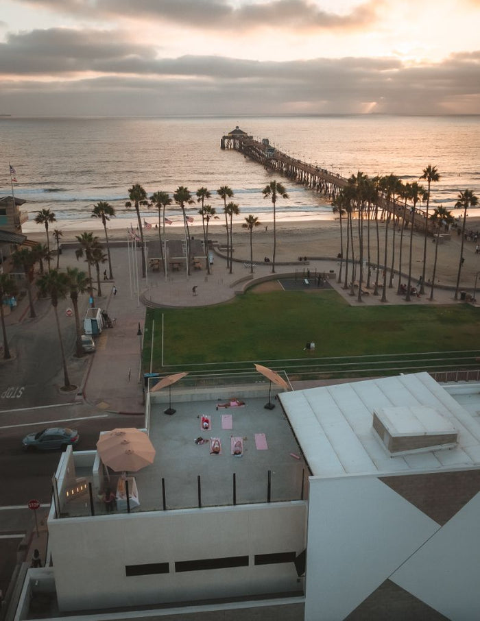 Elevated view of a beach park, ocean pier, and rooftop patio where people are doing pilates at sunset in Imperial Beach, San Diego. - Sip & Social Club San Diego event