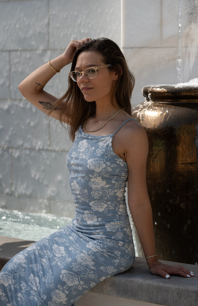 Portrait of Jocelyn, Founder and Creative Director of San Diego event company Sip & Social Club, posing in a blue floral dress and glasses next to an outdoor fountain.