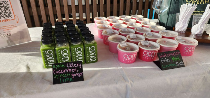 Fresh green juices and cups of watermelon feta salad from Oreka Kitchen displayed on a table at a health and wellness event in San Diego. - Sip & Social Club San Diego event