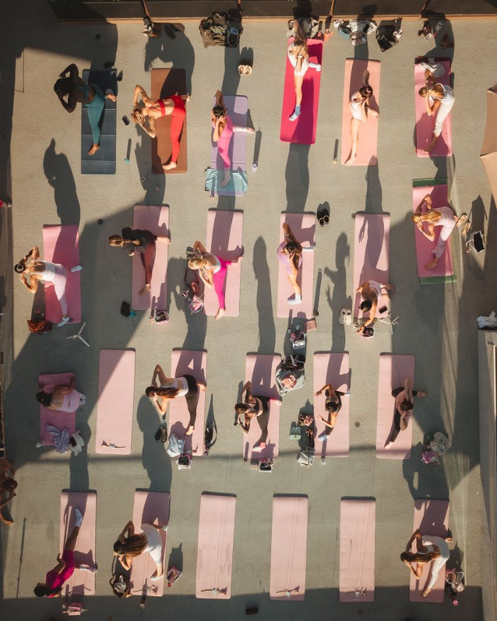Overhead view of a group of women in athletic wear stretching on pink yoga mats during a rooftop pilates class in San Diego. - Sip & Social Club San Diego event