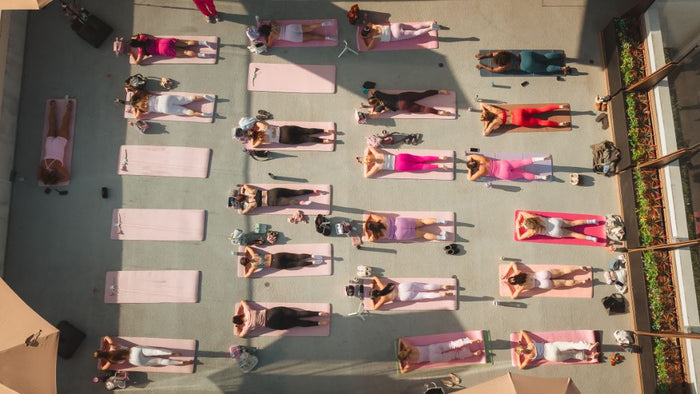 Top-down perspective of participants relaxing on pink mats on a rooftop deck during a Sip and Social fitness event in San Diego. - Sip & Social Club San Diego event