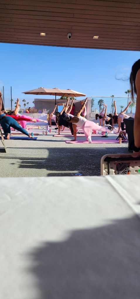 A group of women practicing rooftop pilates leg lifts on pink mats under a clear blue sky in San Diego. - Sip & Social Club San Diego event