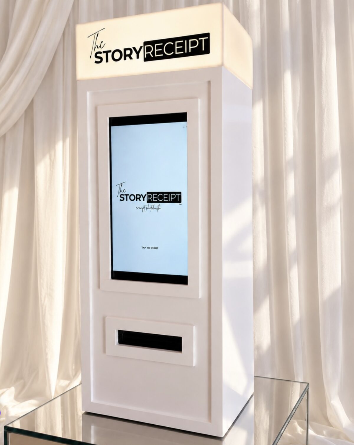 A sleek white receipt photo booth kiosk with a touchscreen, set against cream drapes