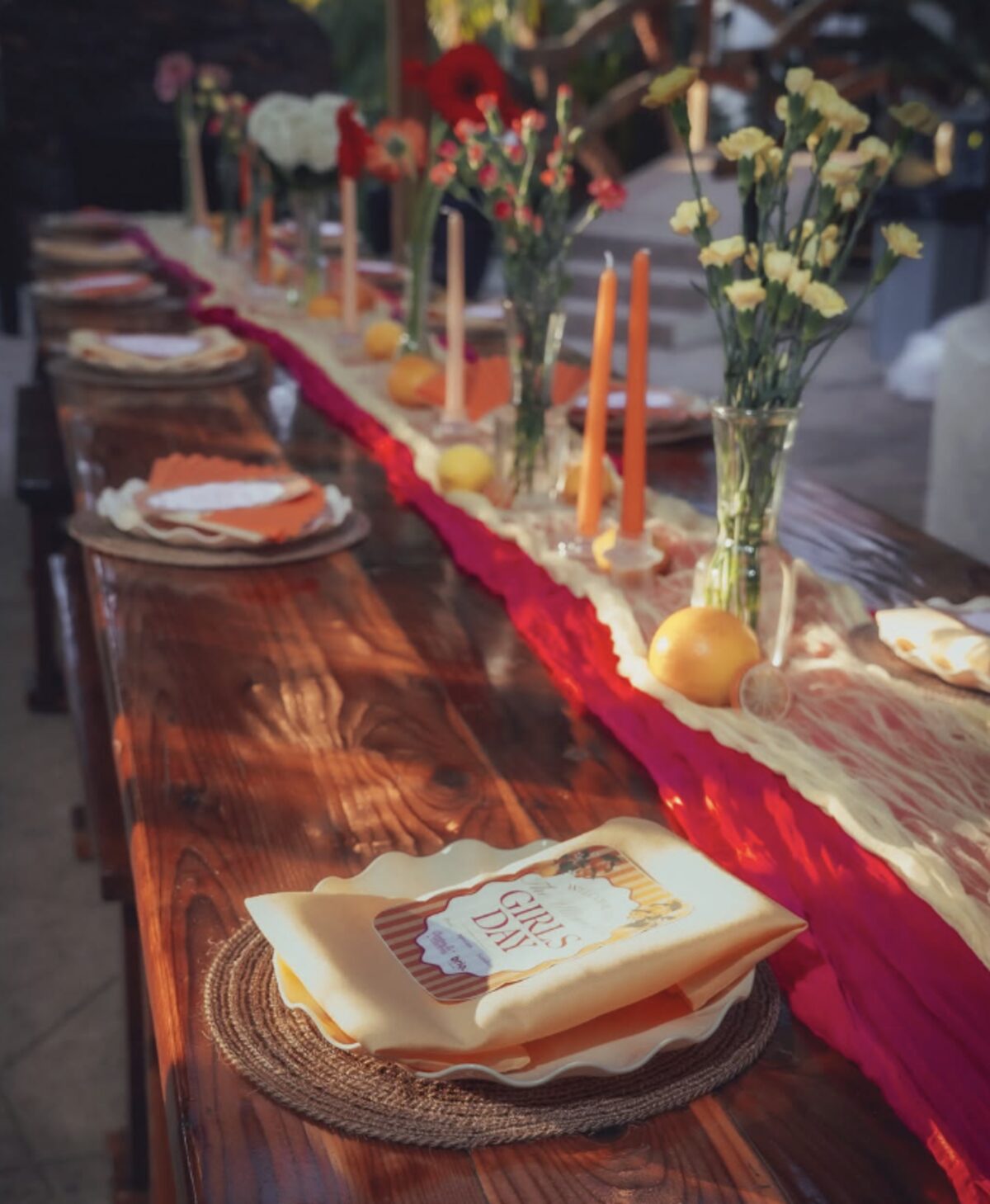 A long table set with orange taper candles, yellow florals, lemons and Girls Day place settings