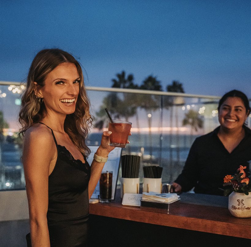 A guest laughing with a cocktail at the rooftop bar at dusk
