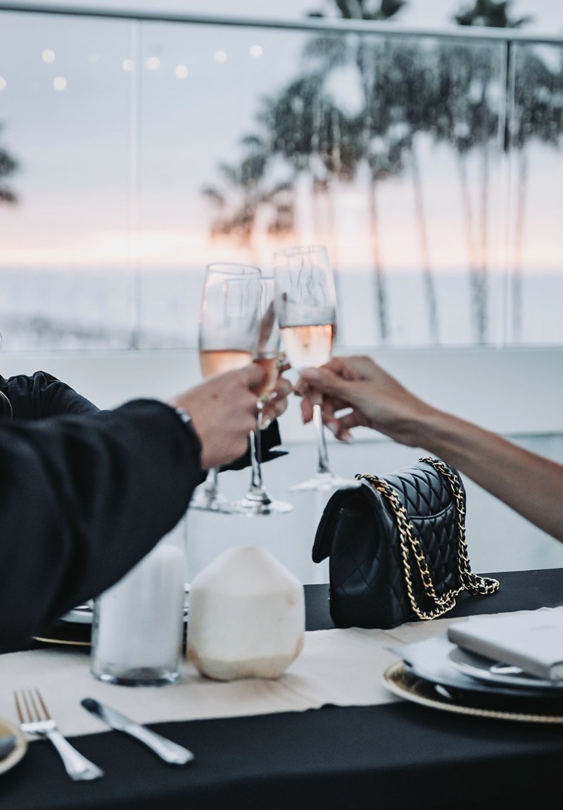 Two guests clinking rosé glasses over a styled dinner table with the ocean behind them
