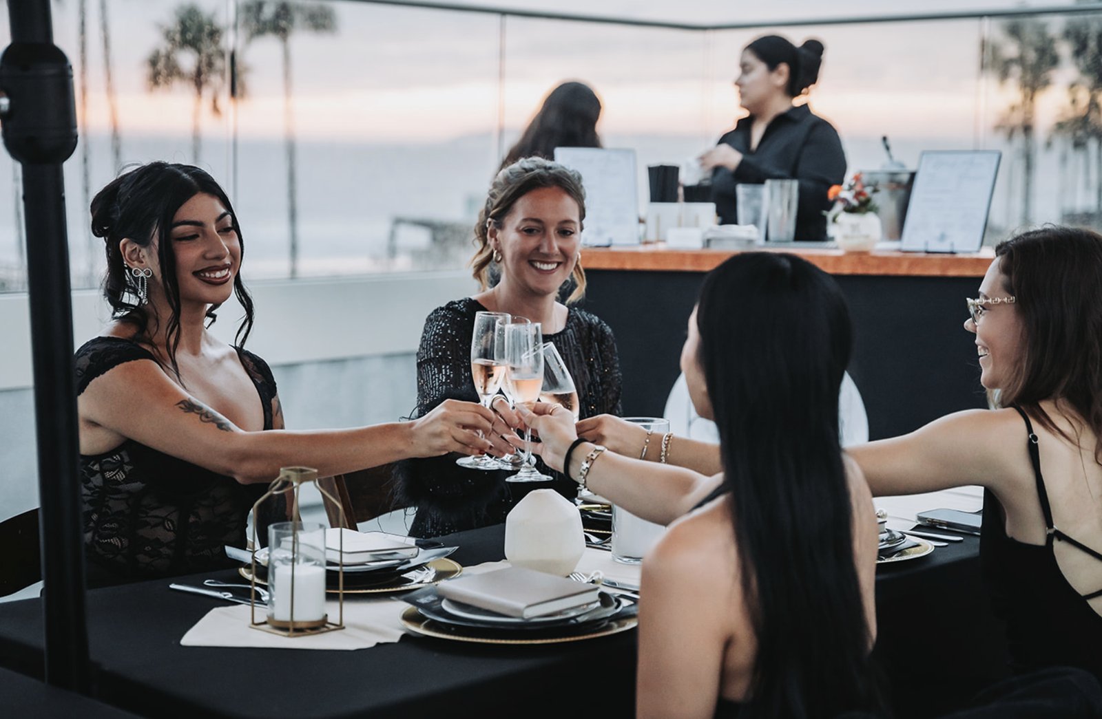 Friends toasting at a black and gold dinner table with the bar and ocean behind them