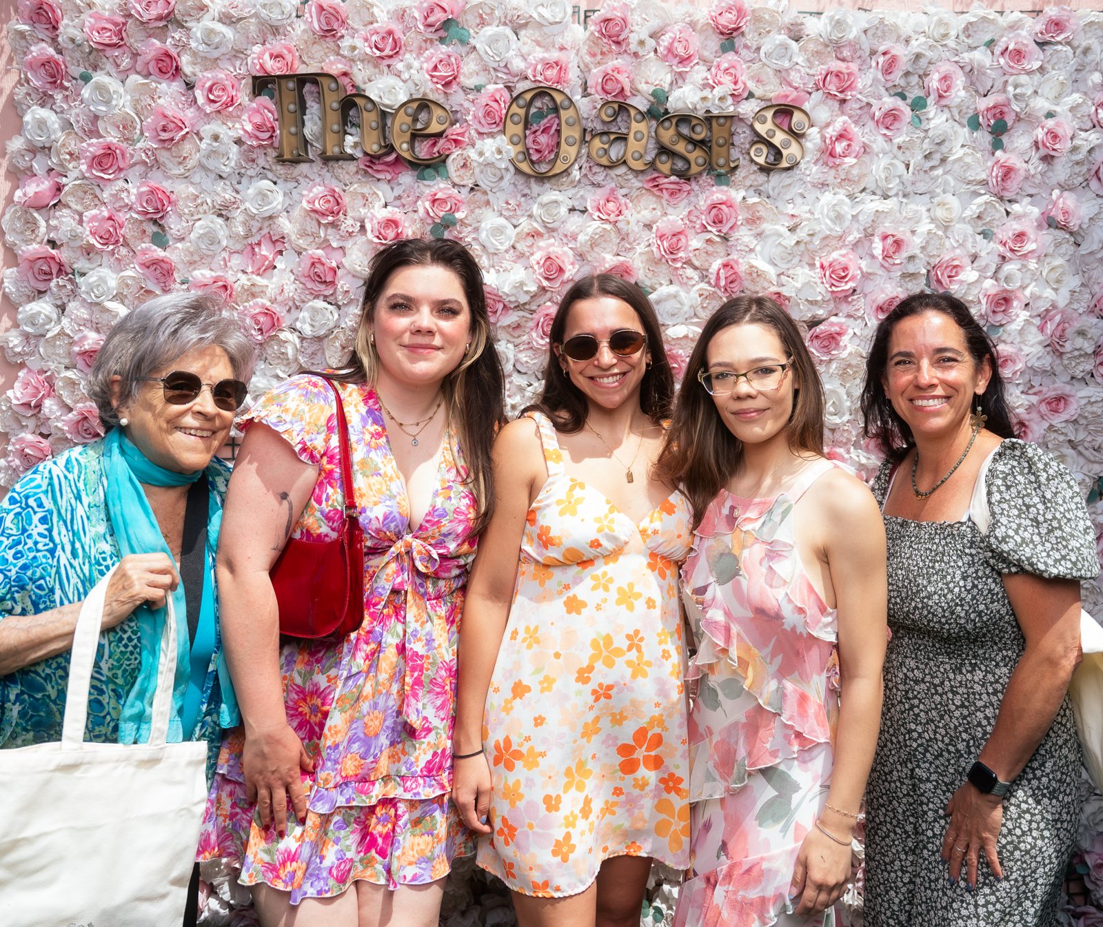 Five women smiling in front of a pink flower wall