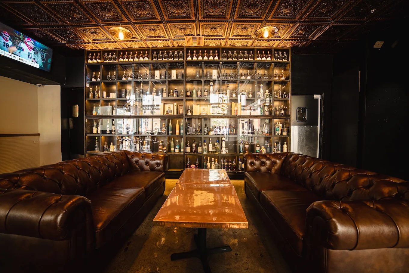 A private lounge with leather chesterfield sofas in front of a lit wall of tequila bottles